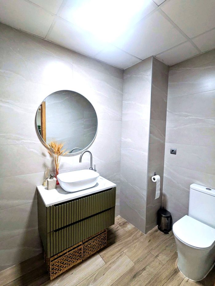 Baño con lavabo, espejo circular y difusor Solatube en el techo